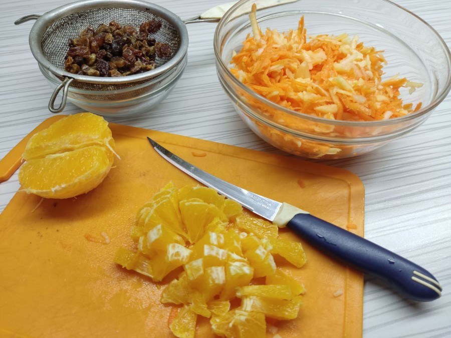 Выложить морковь и яблоко в салатник, добавить нарезанный небольшими кубиками апельсин и изюм